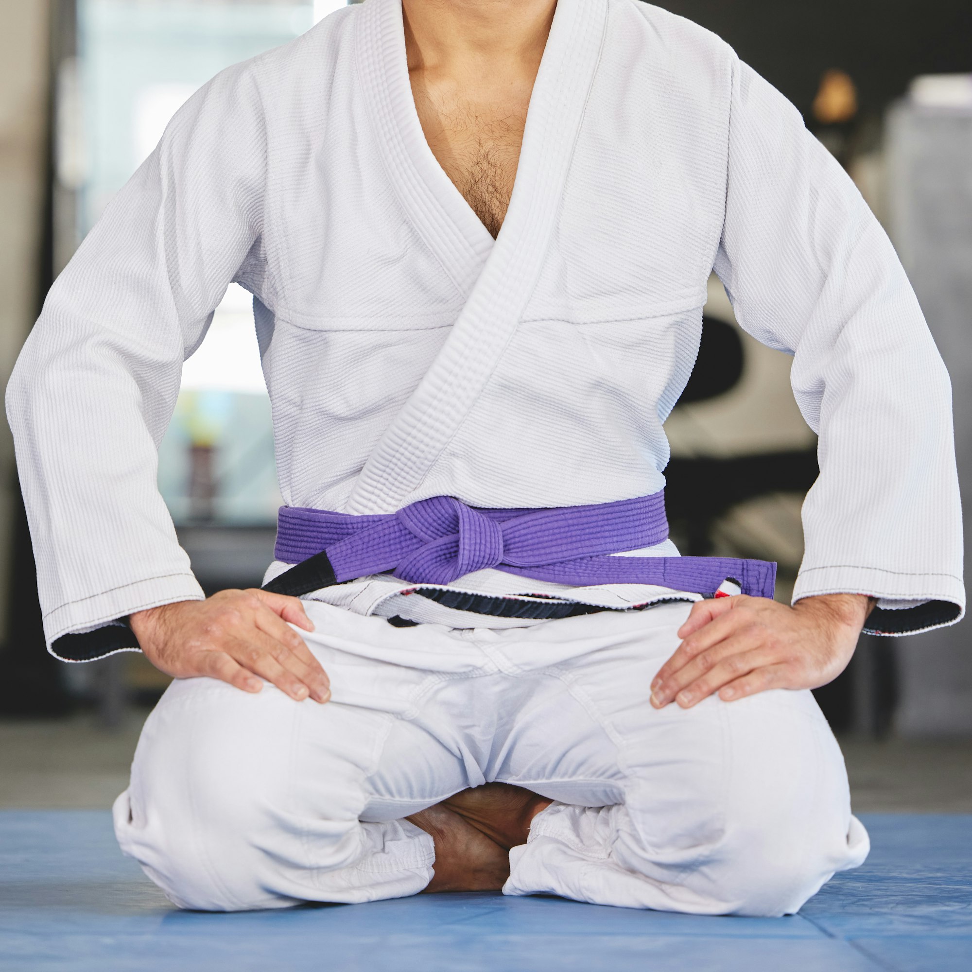 Cropped shot of an unrecognizable young man kneeling in full jiu jitsu gi in the gym