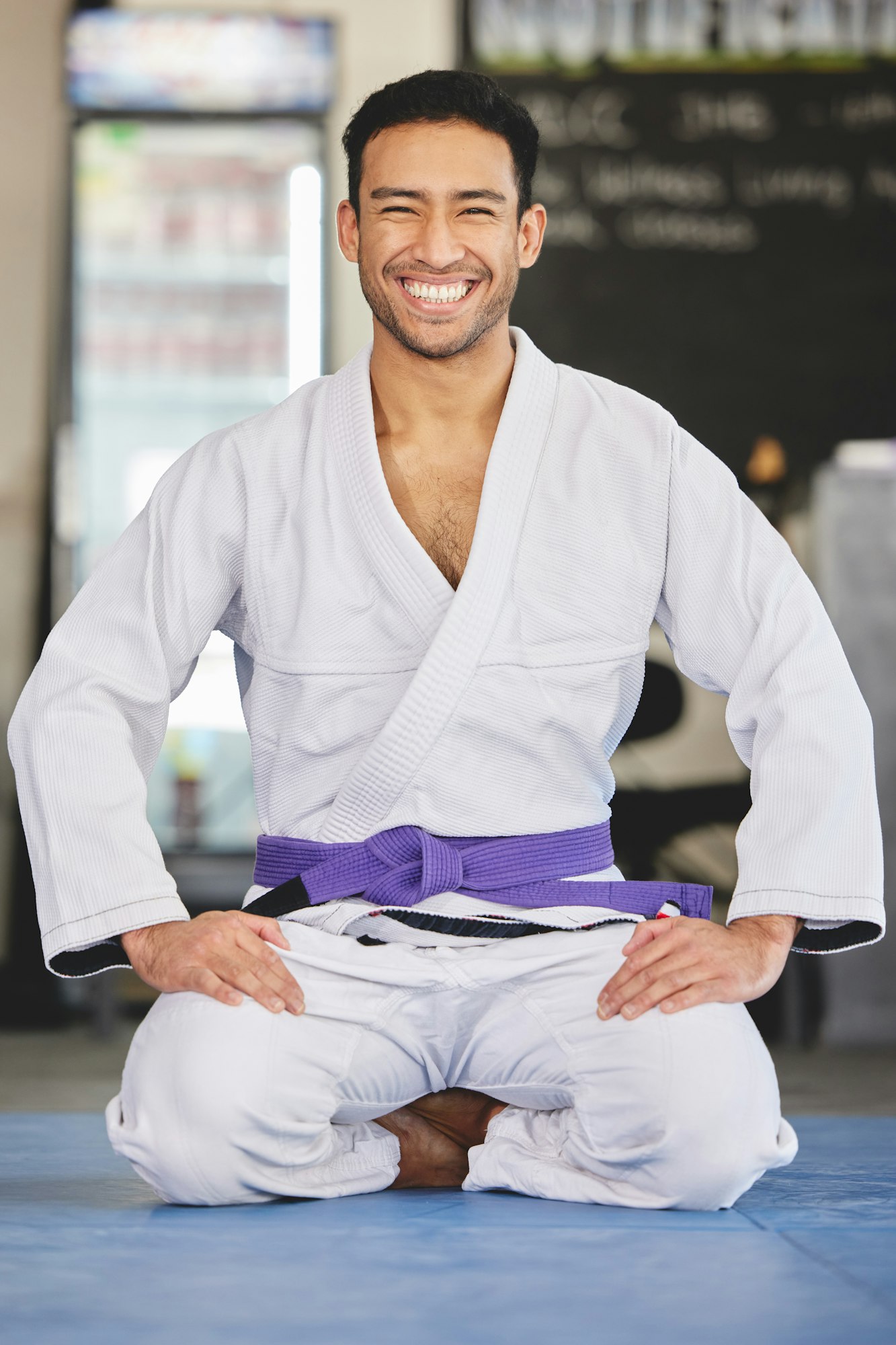 Full length portrait of a handsome young man kneeling in full jiu jitsu gi in the gym